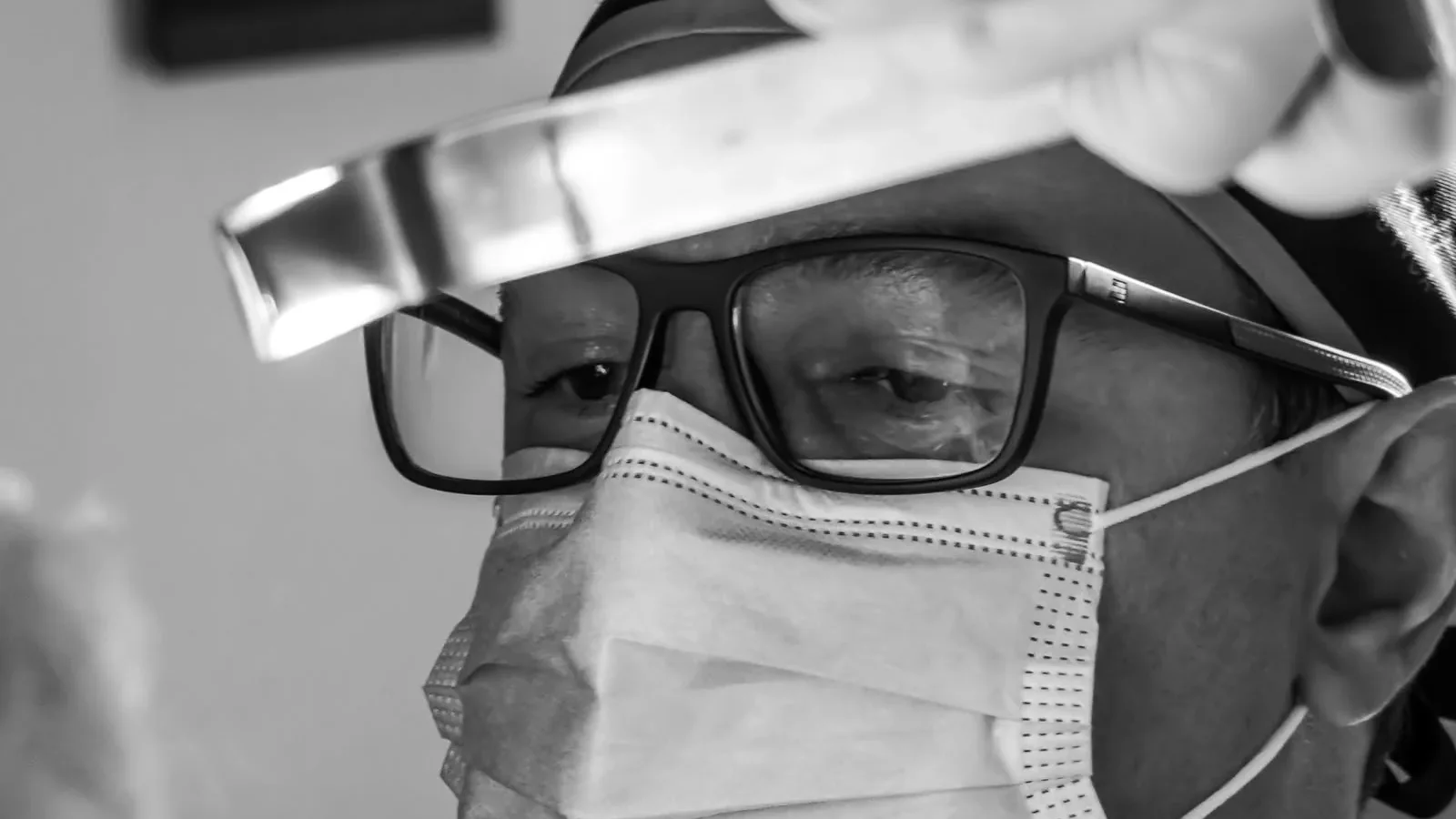 Os olhos do Dr. Lucas Schmidt atrás dos óculos, de máscara, olhando para baixo durante uma cirurgia